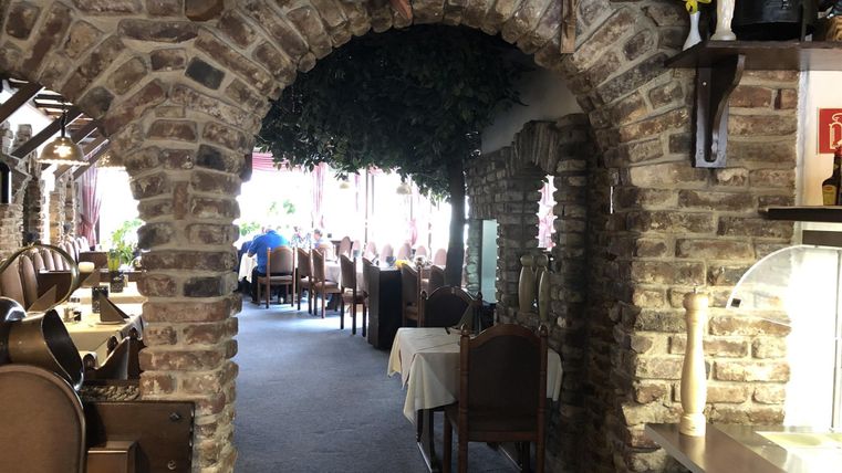 Ein gemütlicher Restaurantbereich mit einem Steinbogen und Holzmöbeln. Der Raum ist hell beleuchtet und bietet eine einladende Atmosphäre.