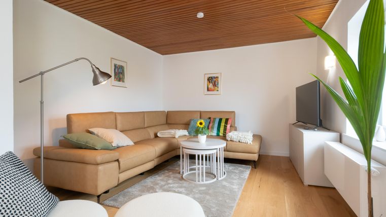 Un salon moderne avec un canapé beige et une table basse. Les murs sont peints en clair, et une plante se trouve dans le coin.