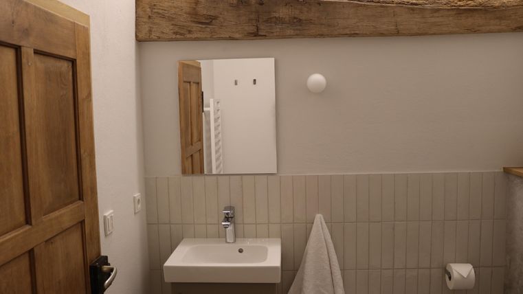 Une salle de bain moderne avec un lavabo simple et un grand miroir. Les murs sont carrelés en clair, et il y a un porte-serviettes et une fenêtre.
