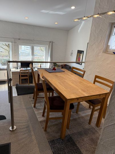 Une salle à manger modernement aménagée avec une table en bois et quatre chaises. De grandes fenêtres laissent entrer beaucoup de lumière et offrent une vue sur l'extérieur.