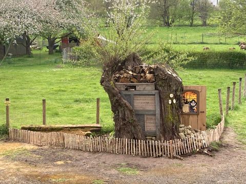 Ein kreatives Baumhaus mit Holzstapel und einem kleinen Eingang. Es steht in einer grünen Wiese, umgeben von einem Holzzaun.
