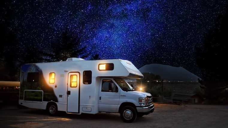 A motorhome stands under a clear starry sky. The night is dark and the sky shines with many stars.