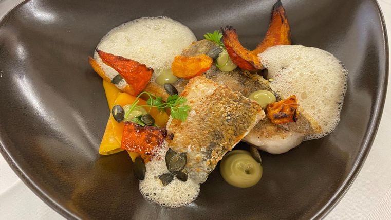 An artfully arranged plate with fried fish, surrounded by colorful vegetables and a creamy foam sauce. The ingredients are lovingly placed, giving the dish an elegant touch.