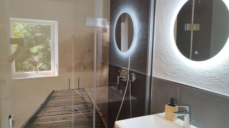 Een moderne badkamer met een douchecabine en een grote spiegel. Door het raam valt daglicht binnen en er is een harmonieuze kleurenkeuze.